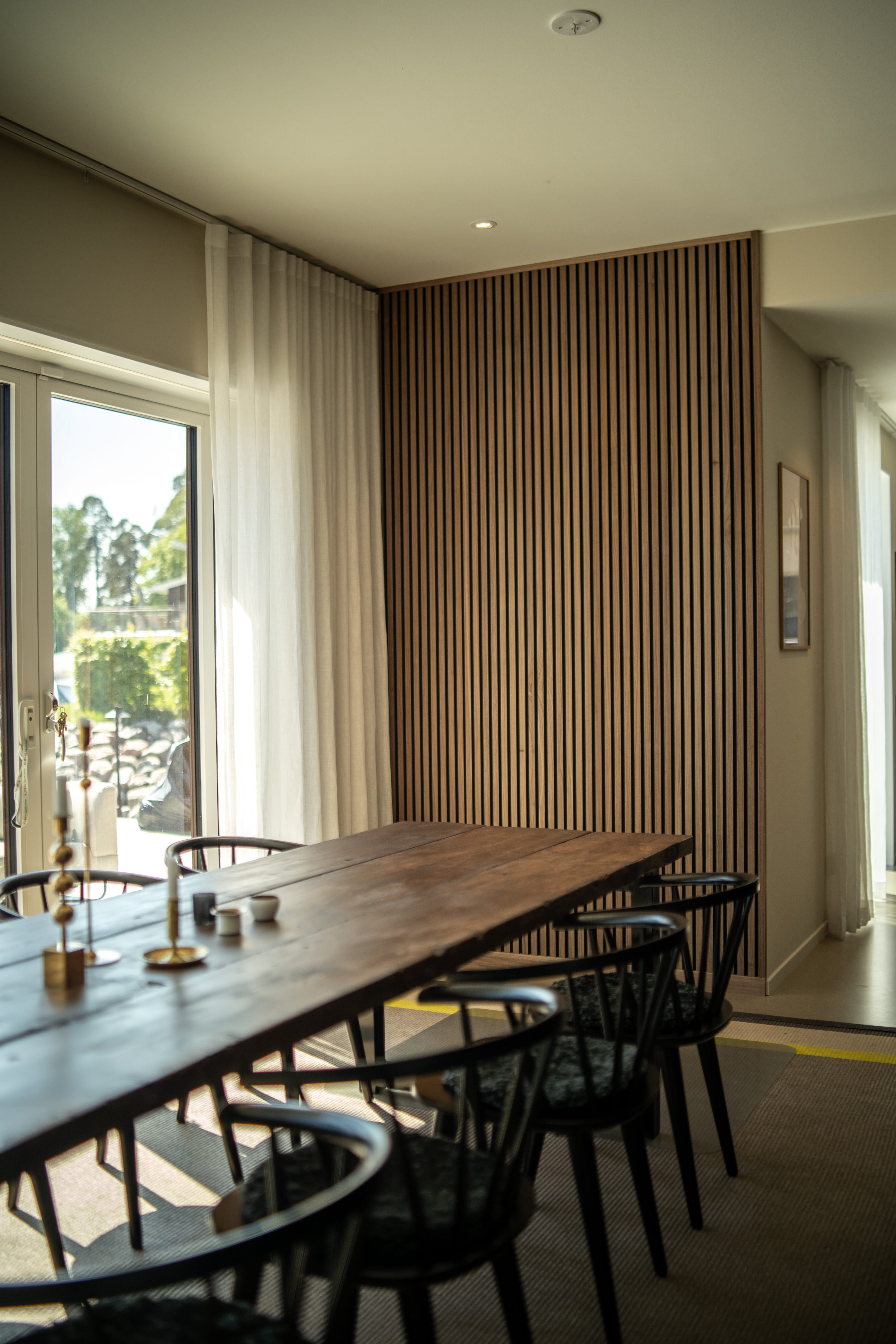 Akupanel wood slat acoustic panel with black backing beside dining table on pale interior wall