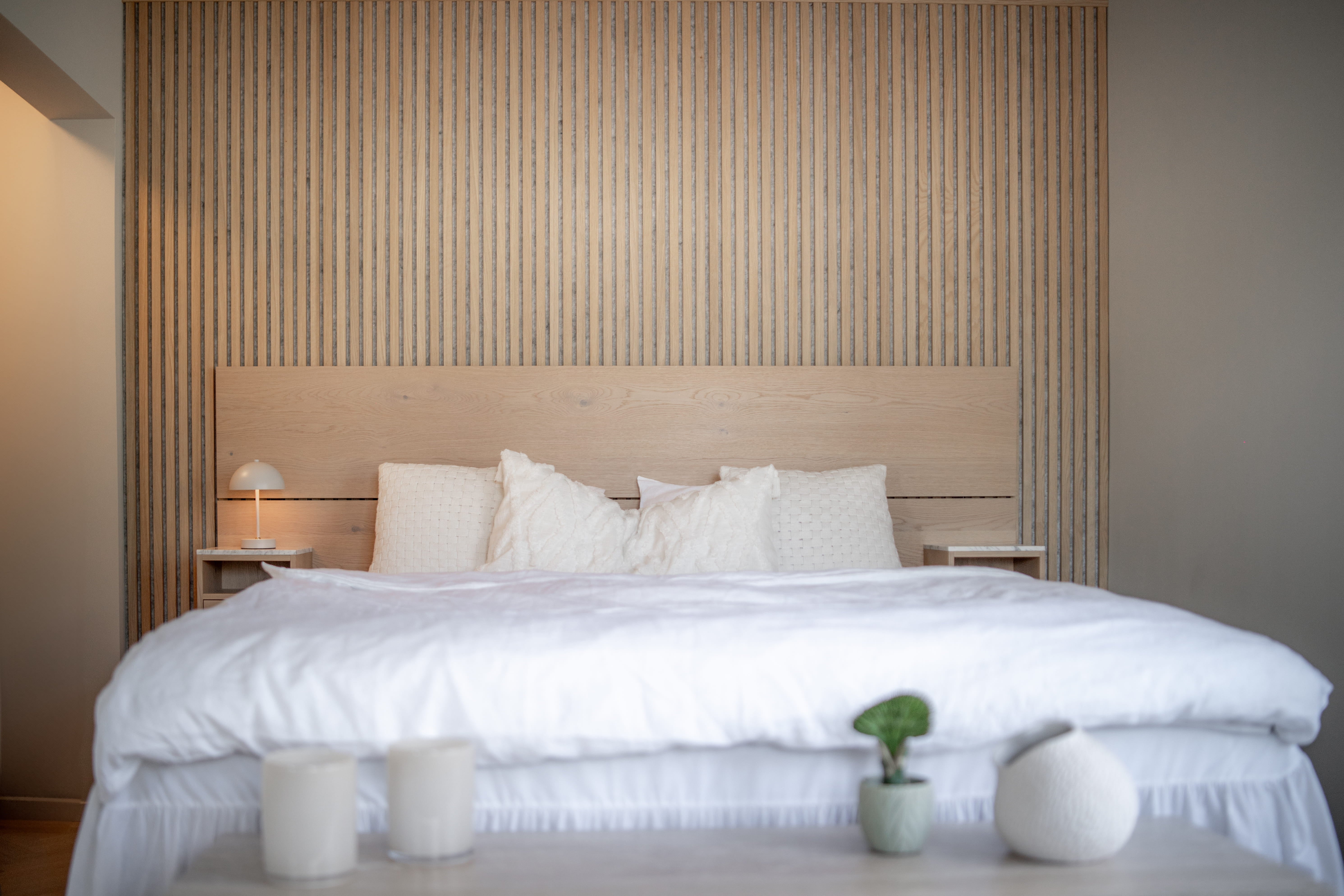 Akupanel wood slat acoustic wall panels with dark backing behind a bed and headboard on neutral walls.