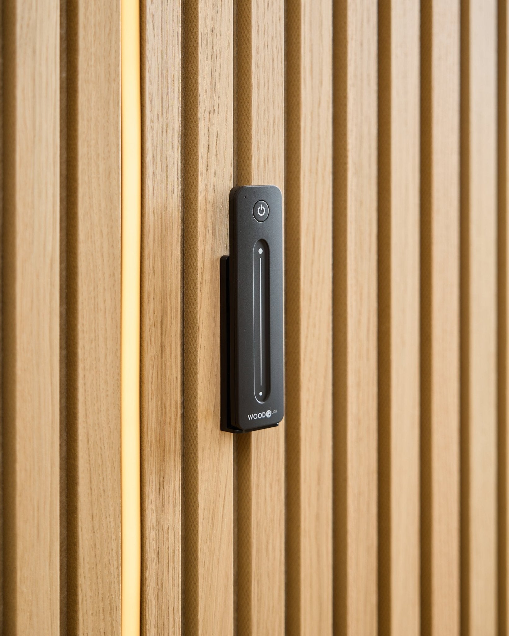 Black remote control mounted on light wood Akupanel slat wall with vertical warm LED strip