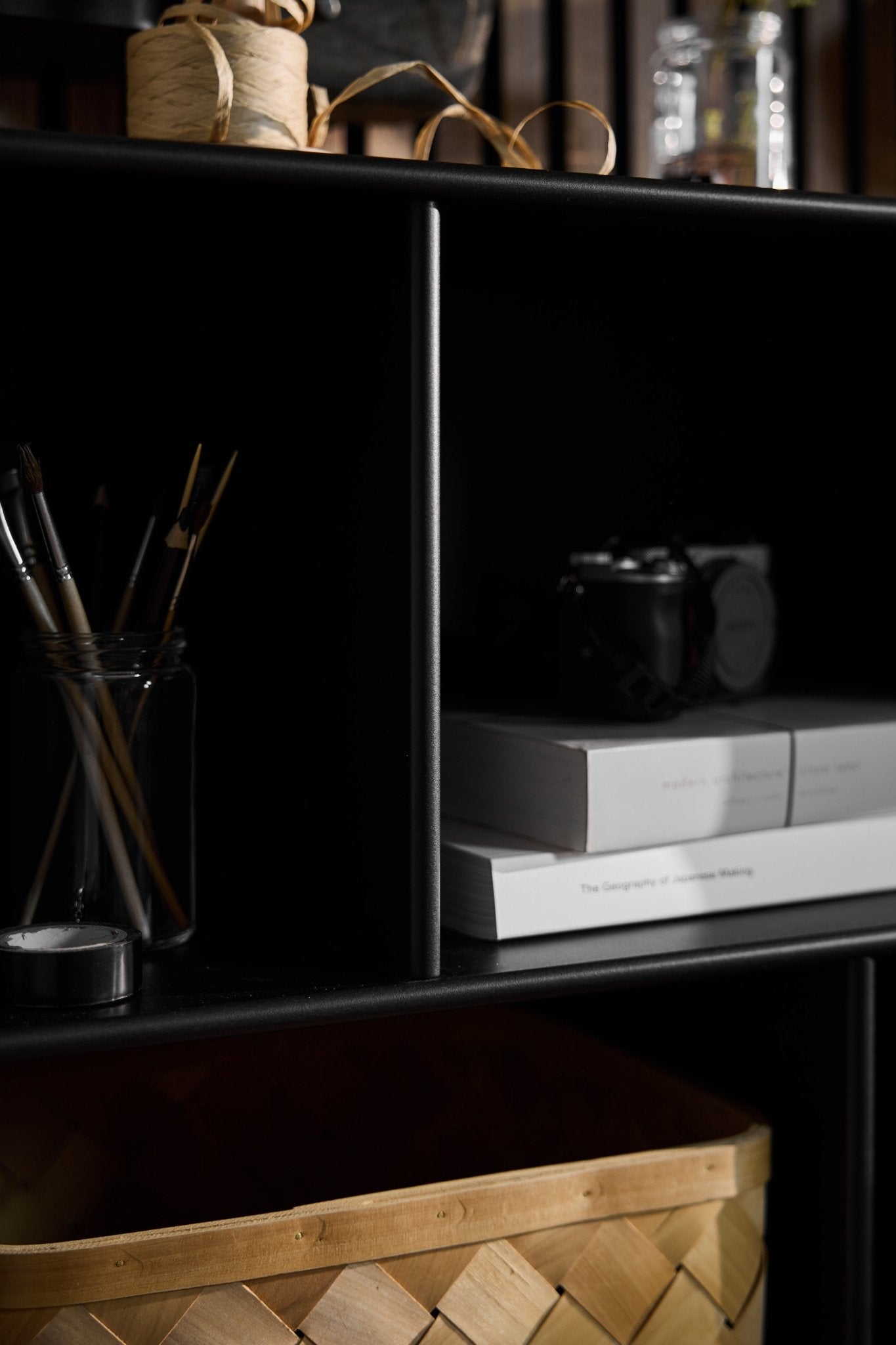 WoodUpp Arka open black cabinet with jars, books, camera, basket, and twine arranged on shelves in a softly lit Nordic-style room.