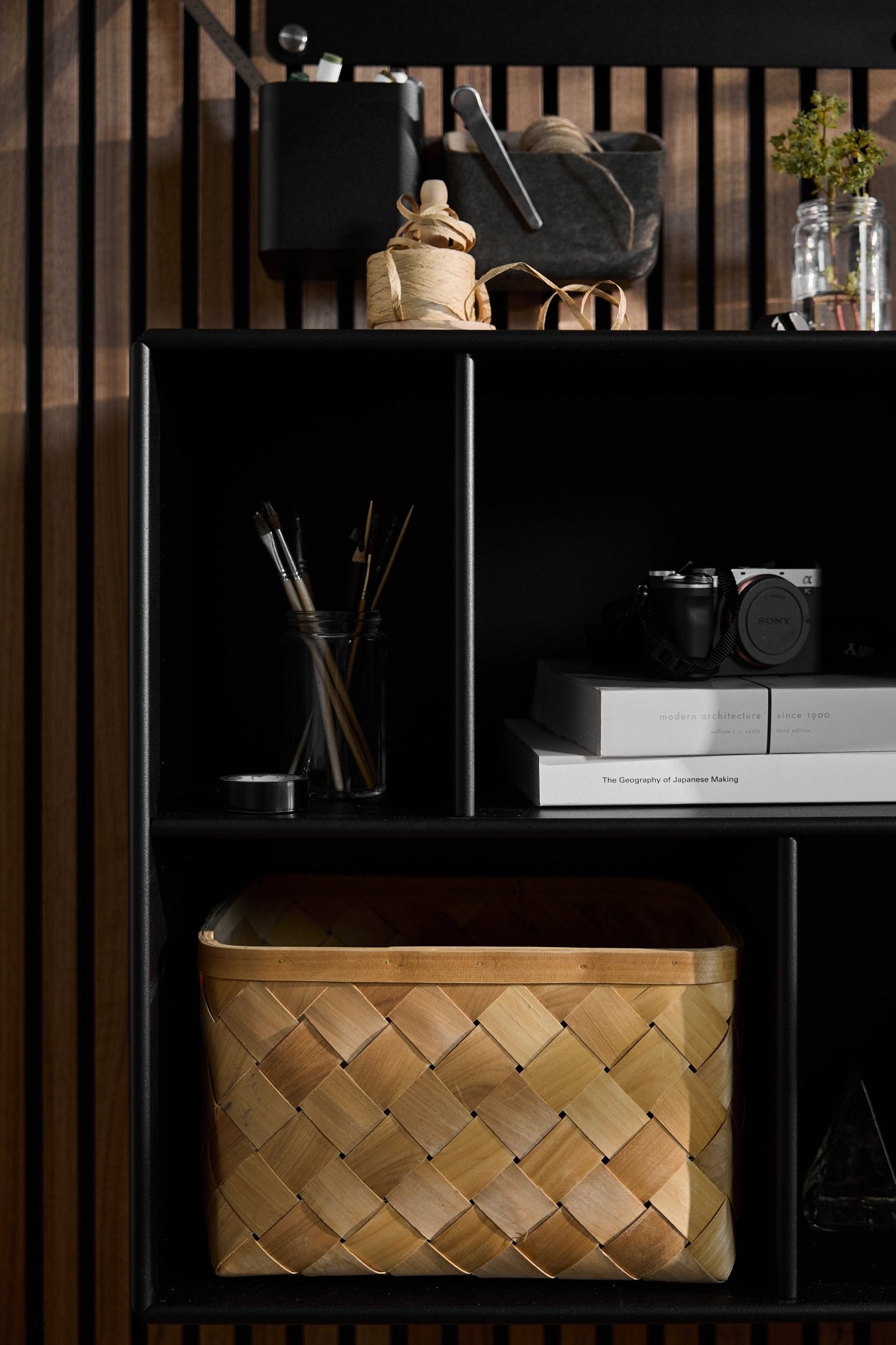 Arka | Open Cabinet / Black by WoodUpp holds art supplies, books, a camera, and a basket against a Nordic Akupanel acoustic slatwall backdrop.