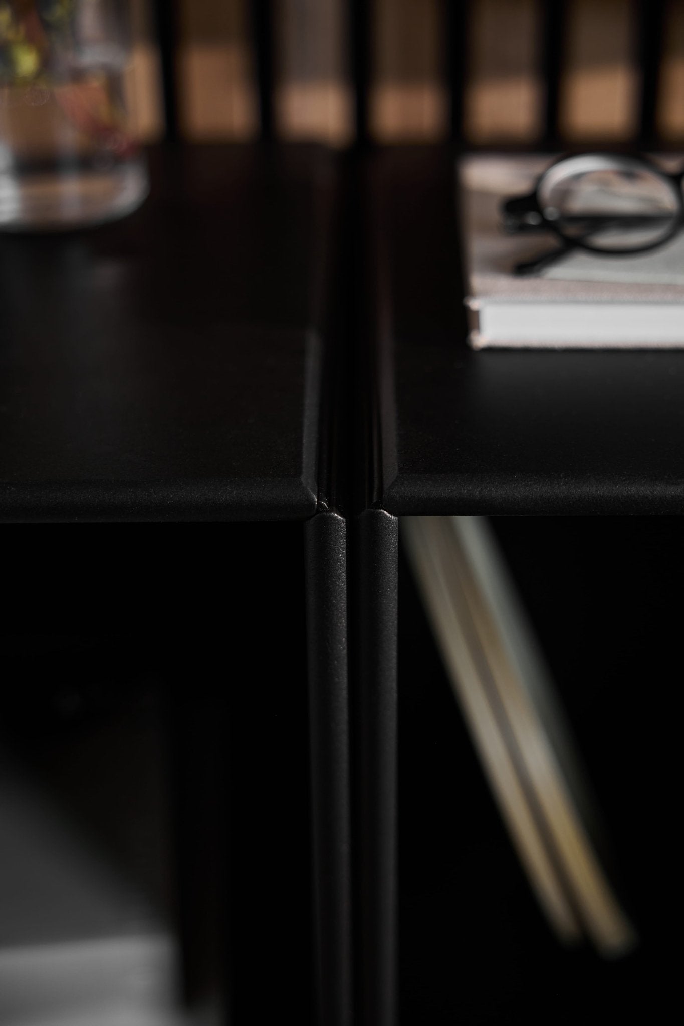 Close-up of Arka | Open Cabinet / Black acoustic wood panel by WoodUpp; glasses and book on the right, glass of water left, Danish furniture styling.