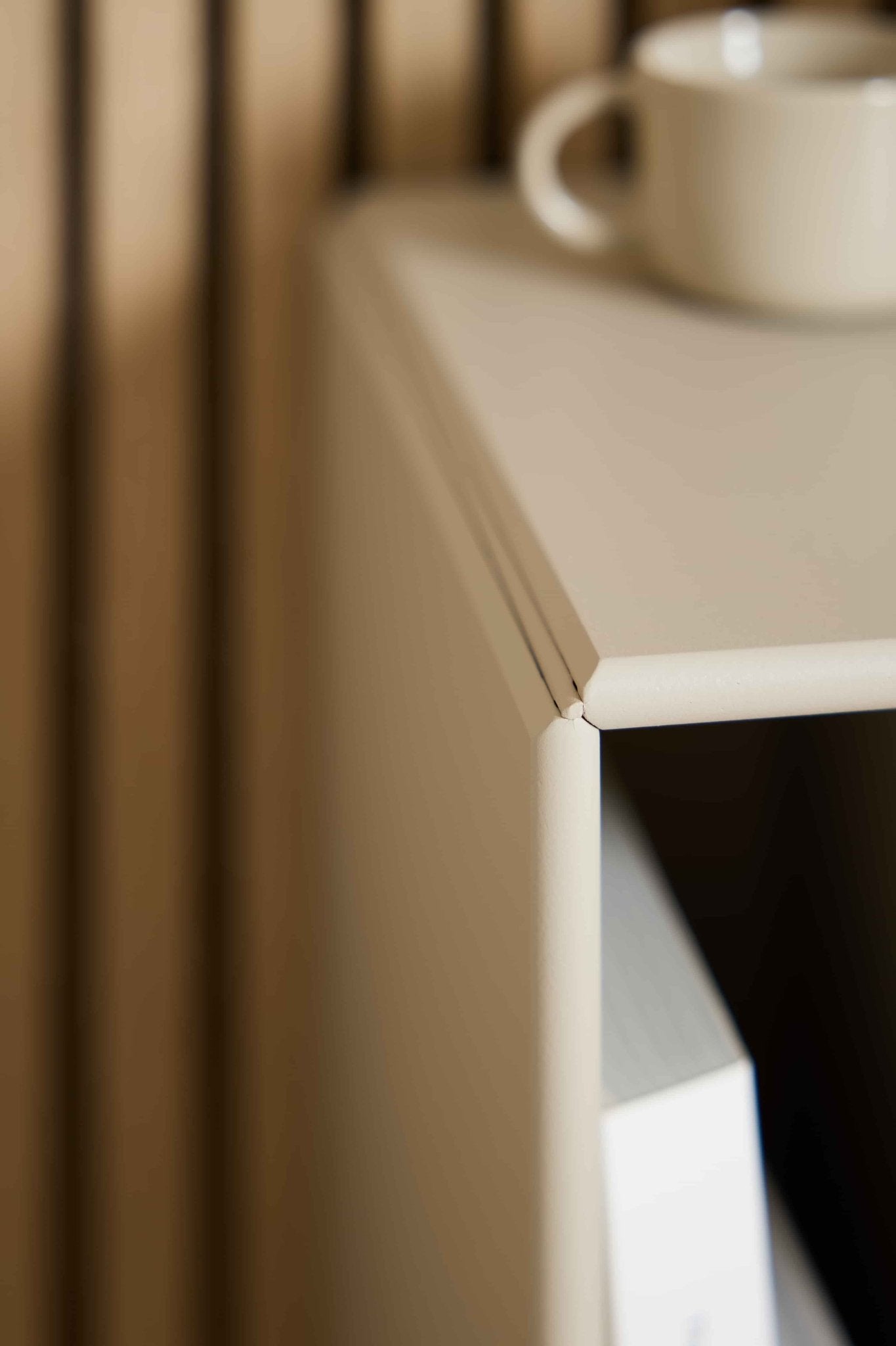 Close-up of the Arka | Bookcase in Beige by WoodUpp with a white cup on top, a book inside, and vertically lined acoustic panels in the background.