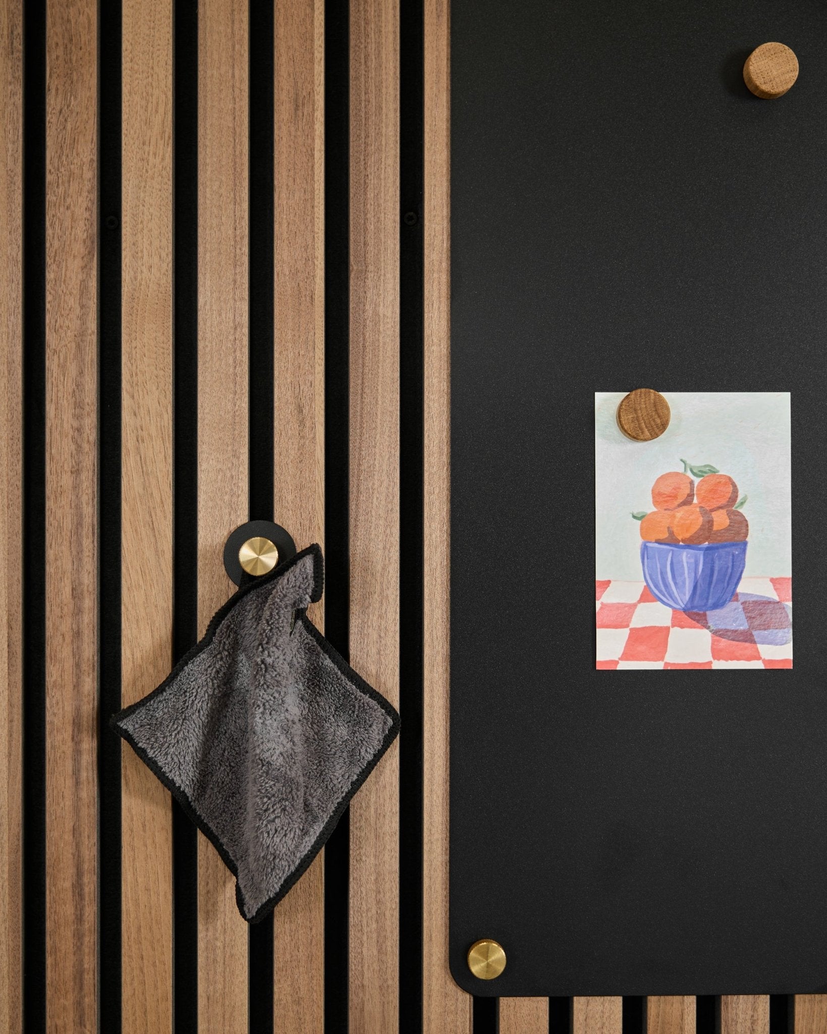 Akupanel wood slat acoustic wall with black magnetic board holding a postcard with wooden magnets, towel on brass hook