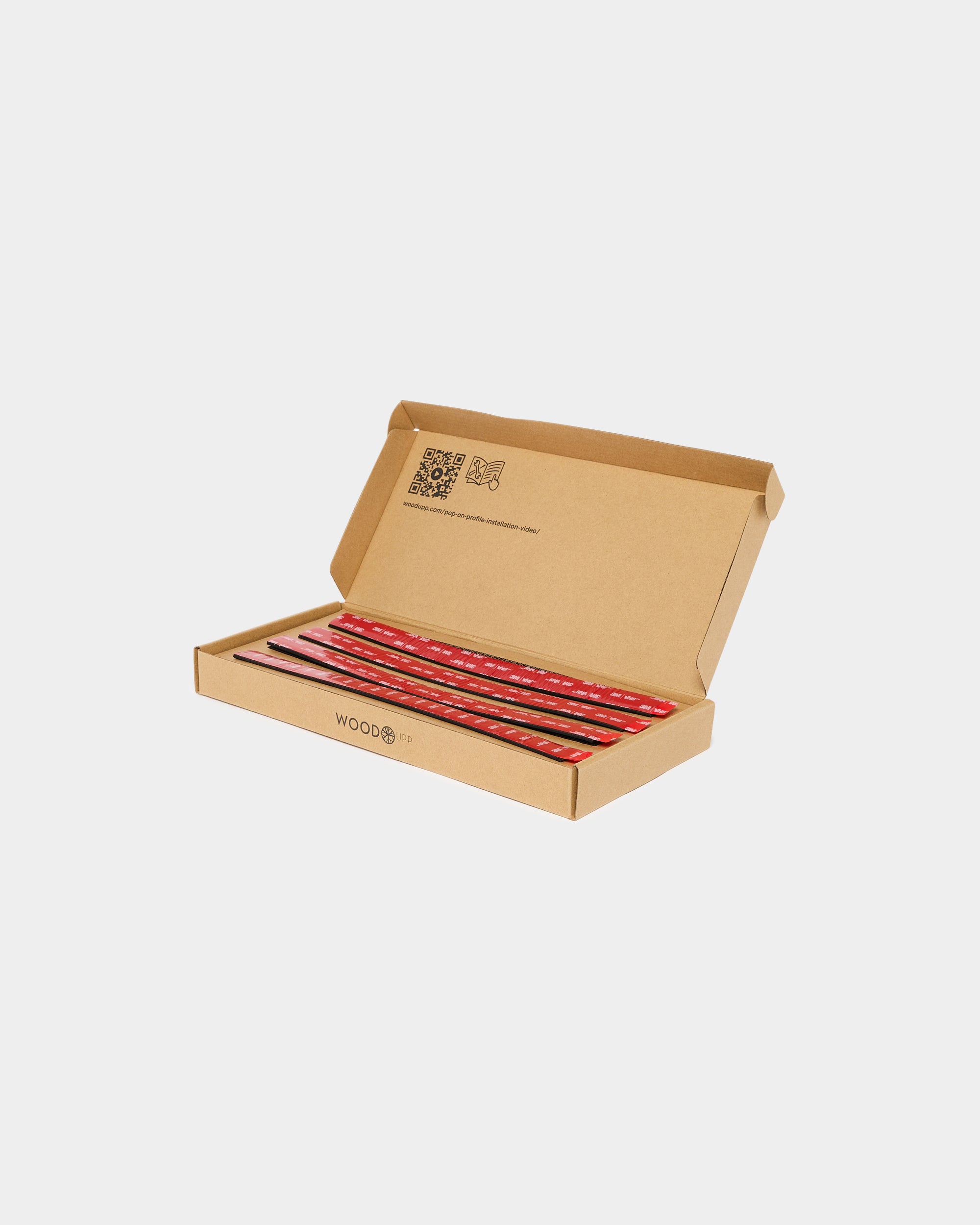 Open cardboard box containing red adhesive mounting strips on a plain white background