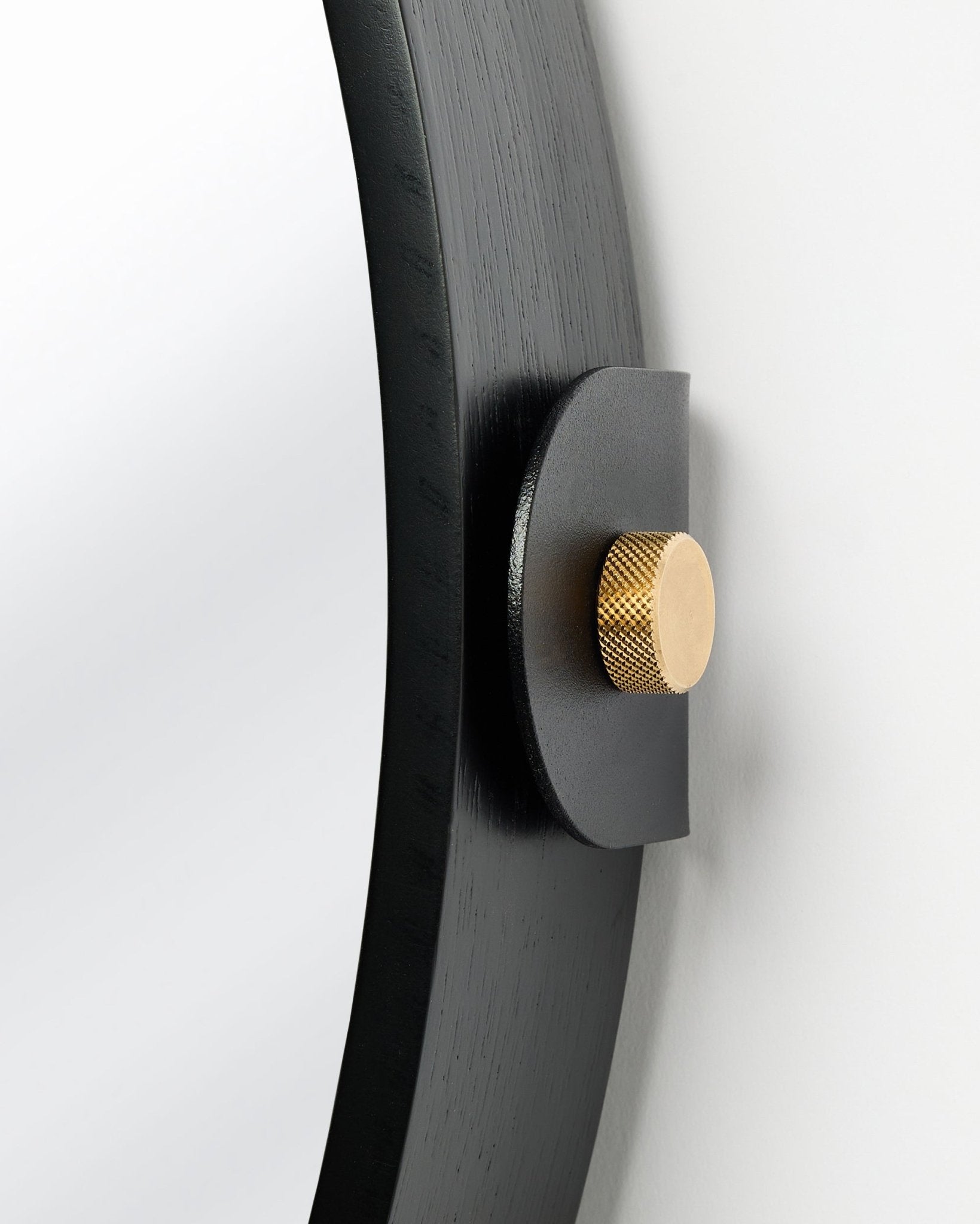 Close-up of Linn mirror black oak frame and gold knurled mounting knob on a white wall
