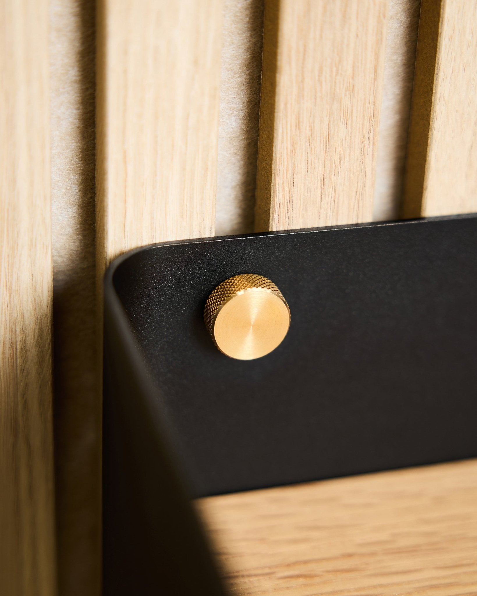 Brass finger screw on black bracket mounted on light wood Akupanel slat panel