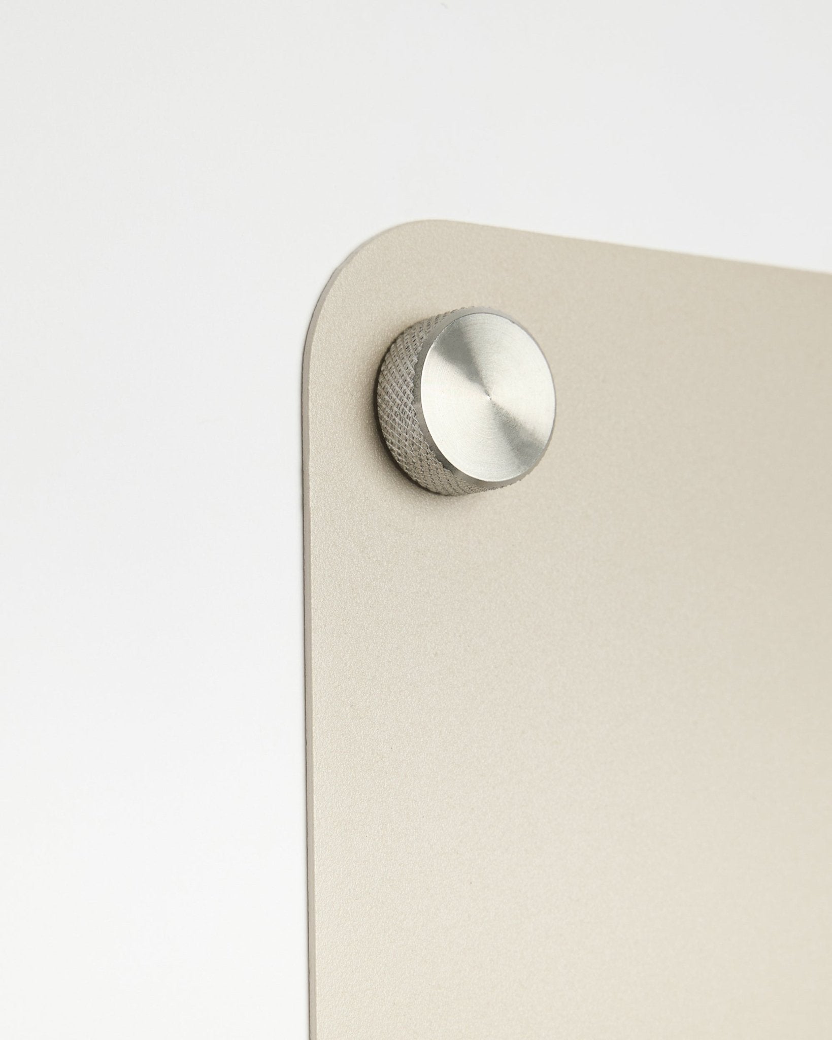 Round metal knob with knurled edge on beige Norr magnetic board, plain white background.