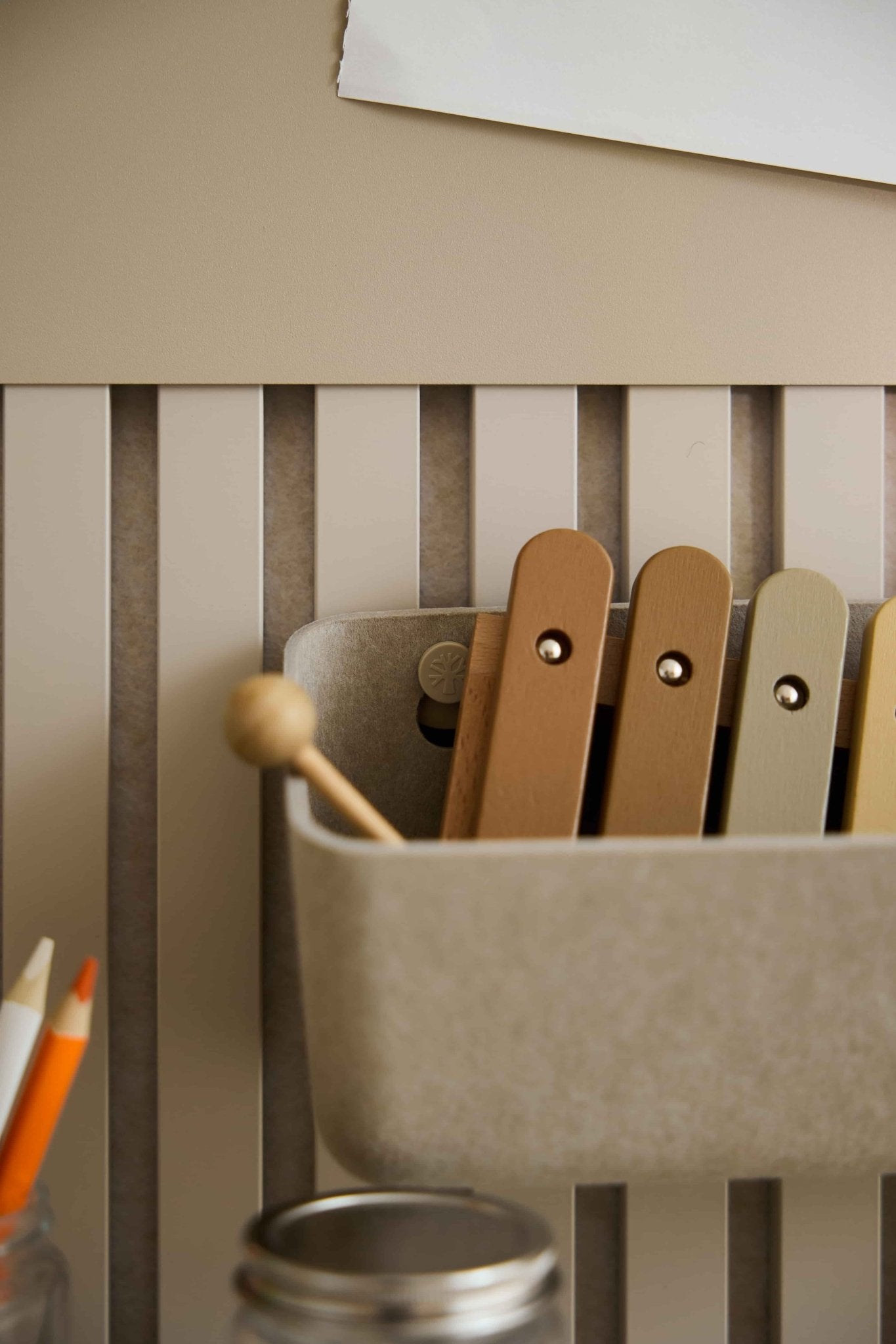 Close-up of a neutral xylophone and pencils in front of a WoodUpp Beige Akupanel acoustic slatwall panel with striped texture.