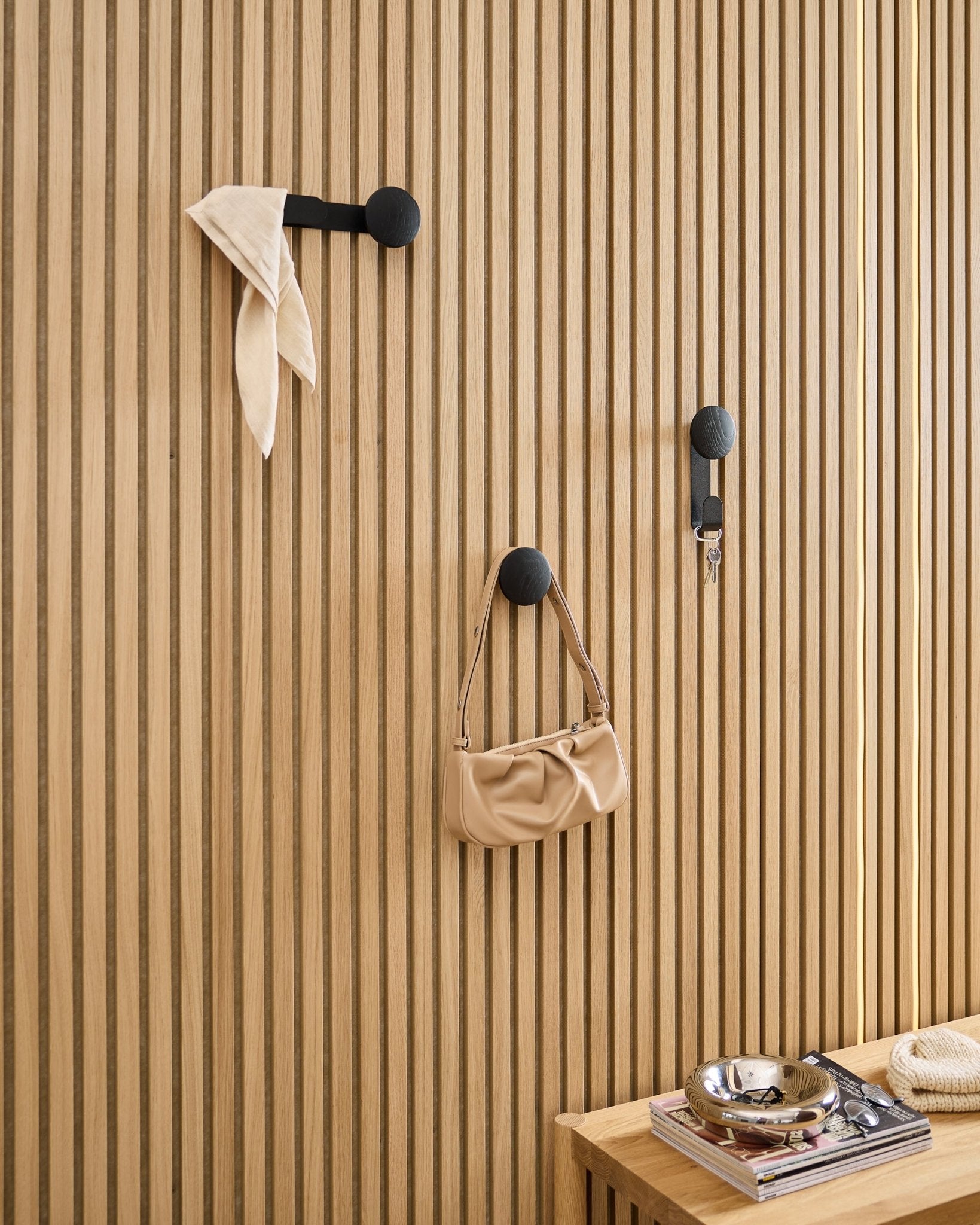 Black Linn hangers on oak Akupanel slat wall holding scarf, keys and beige bag.