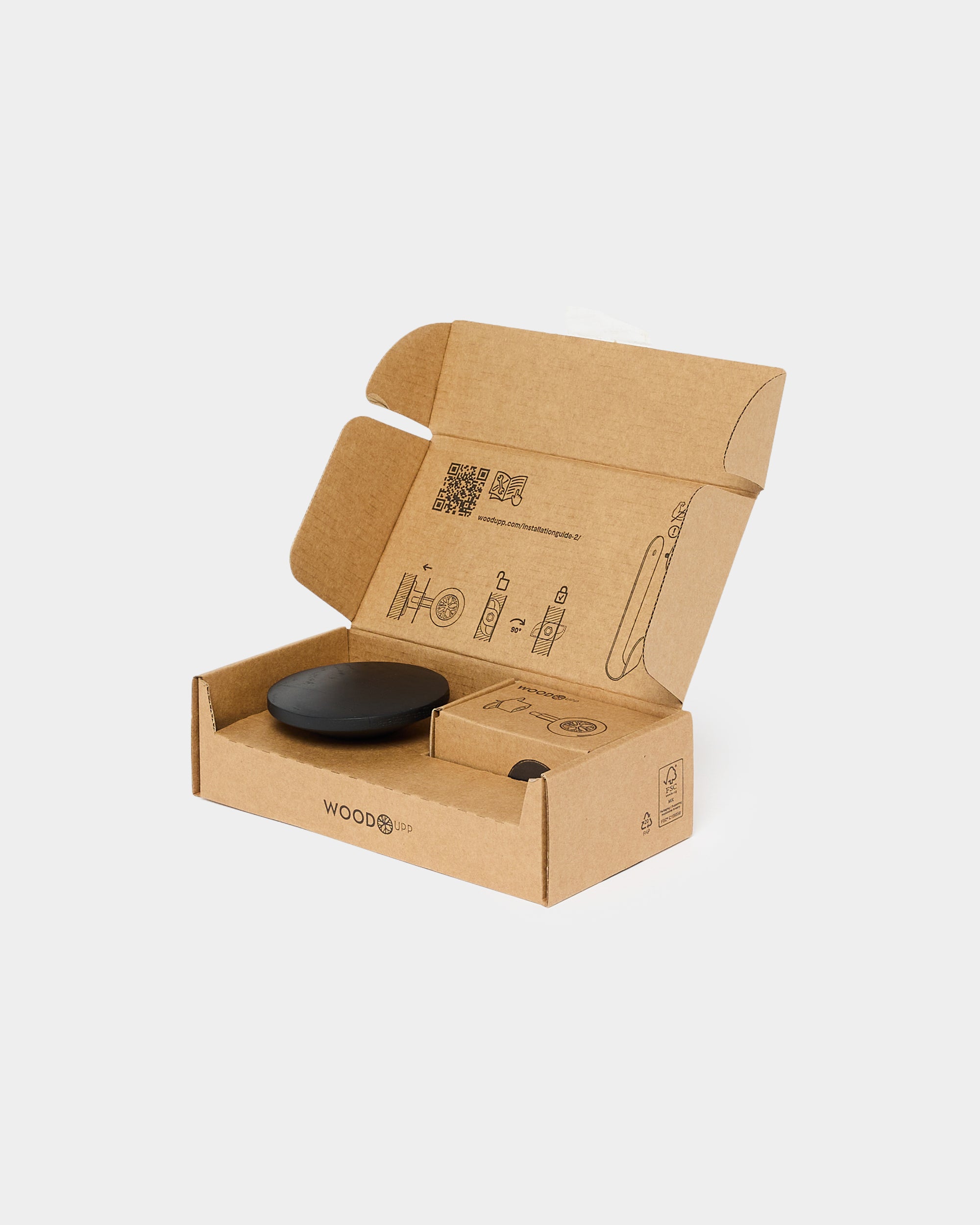 Black round accessory inside an open WoodUpp cardboard box with printed instructions on the inner lid