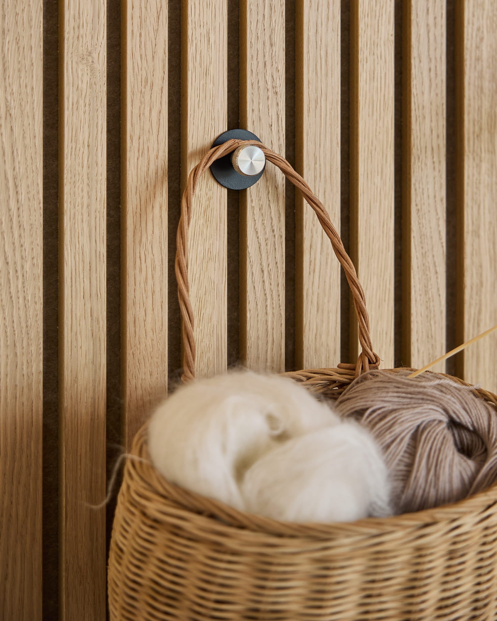 Norr coat hook X1 black/stainless mounted on Akupanel acoustic slat wall, wicker basket and yarn in foreground
