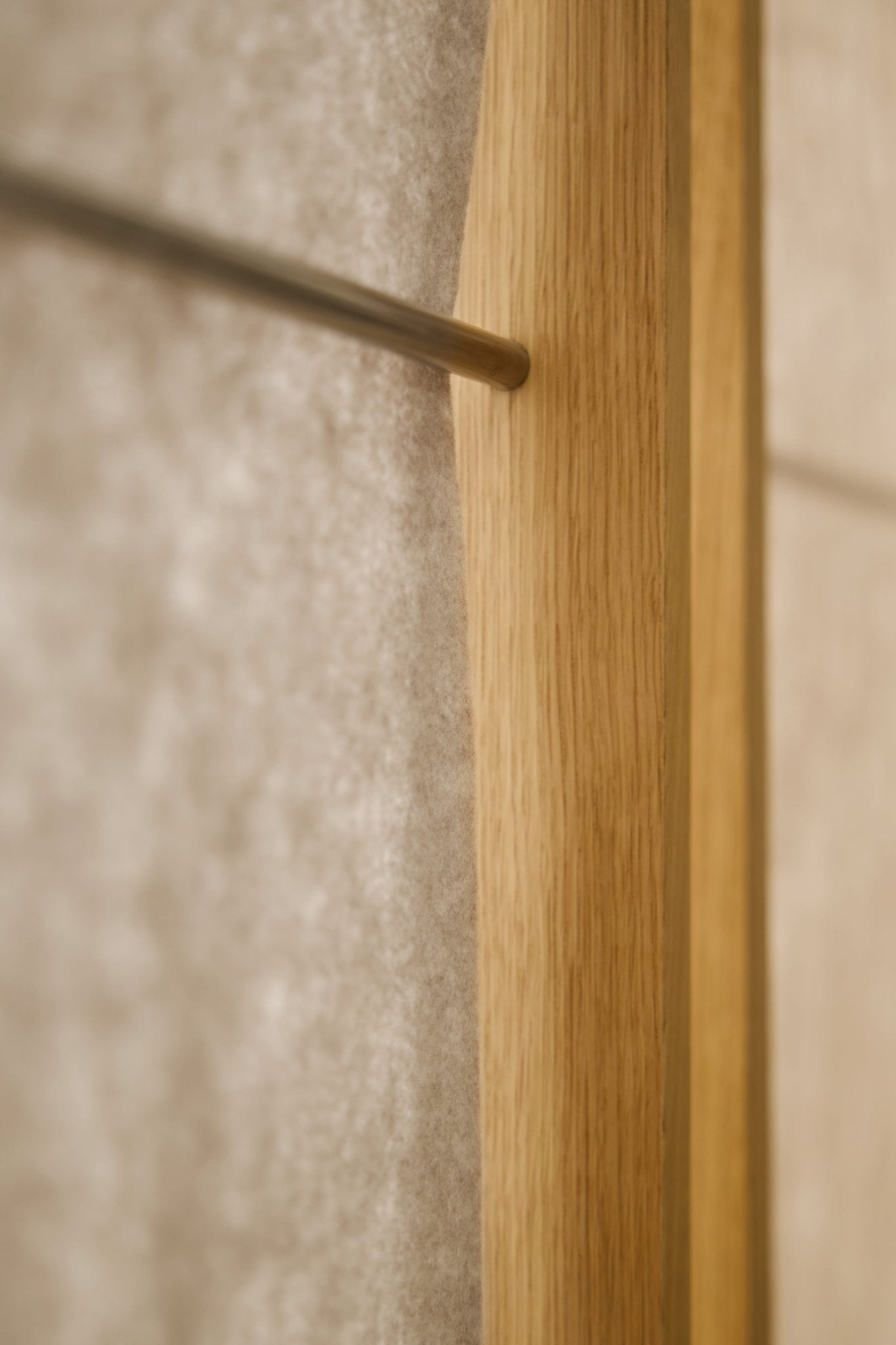 Close-up of a metal rod mounted on a beige wall next to acoustic wood, shown with WoodUpp Vigg Felt Sheet (58x176 cm, Light Beige) as a room divider.