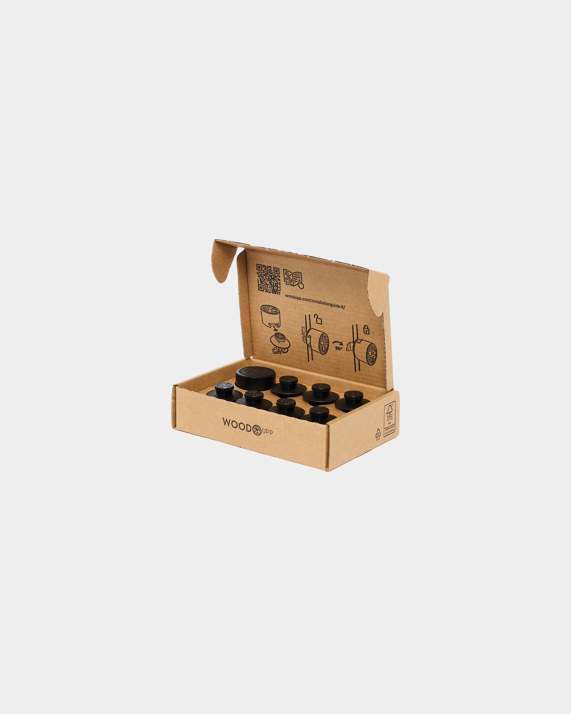Open cardboard box with black plastic mounting caps and printed installation instructions inside lid, plain white background