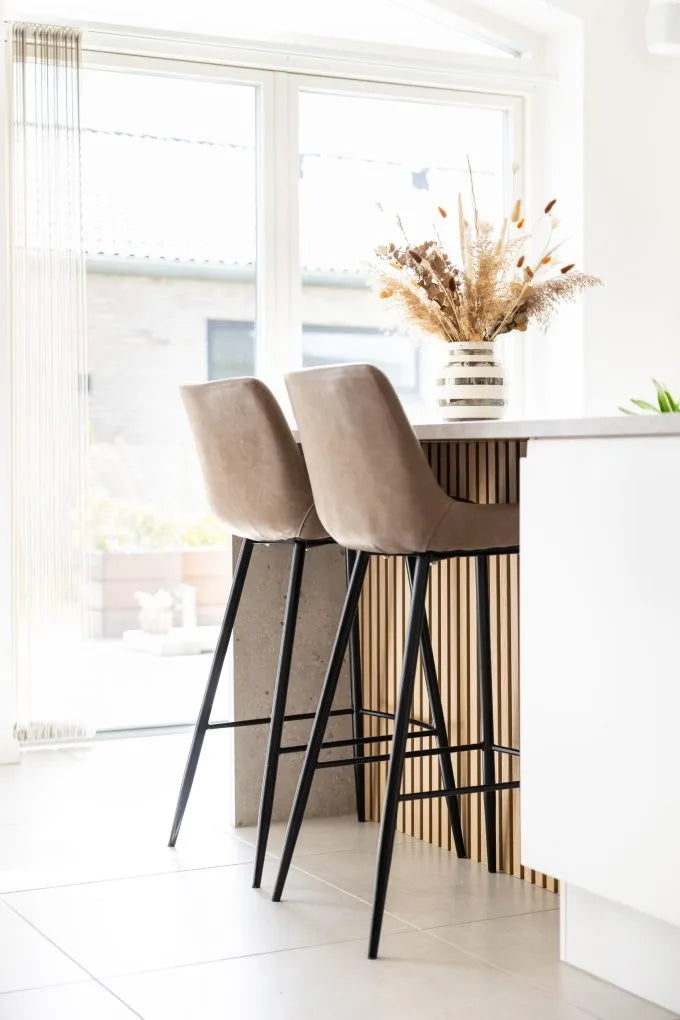 Beige bar stools at a kitchen island with Akupanel vertical wood slat front and a vase of dried flowers
