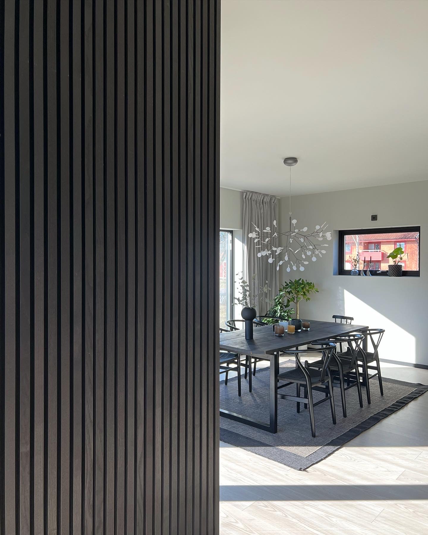 Black Akupanel acoustic slat wall panels adjacent to a sunlit dining room with table and chairs.