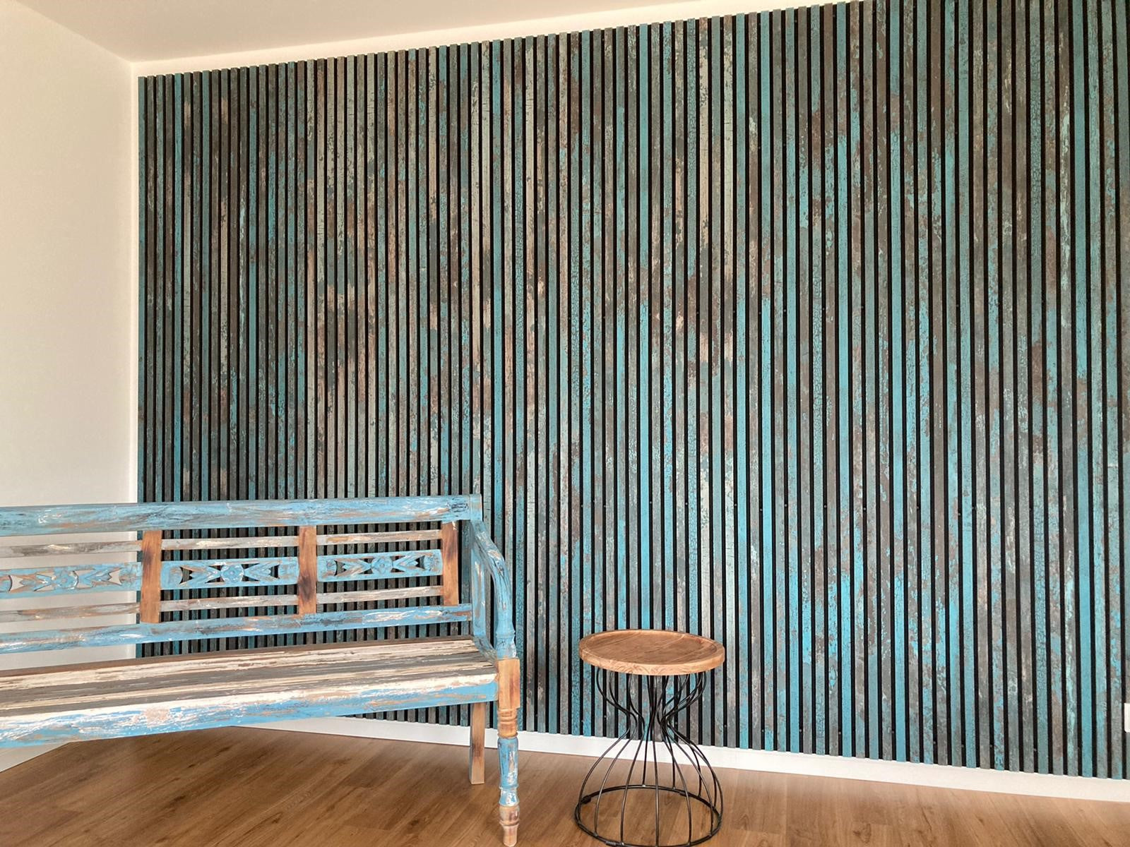 A rustic wooden bench and round table sit beside a blue and brown acoustic slatwall panel on a wooden floor in a bright, modern Nordic-inspired space.