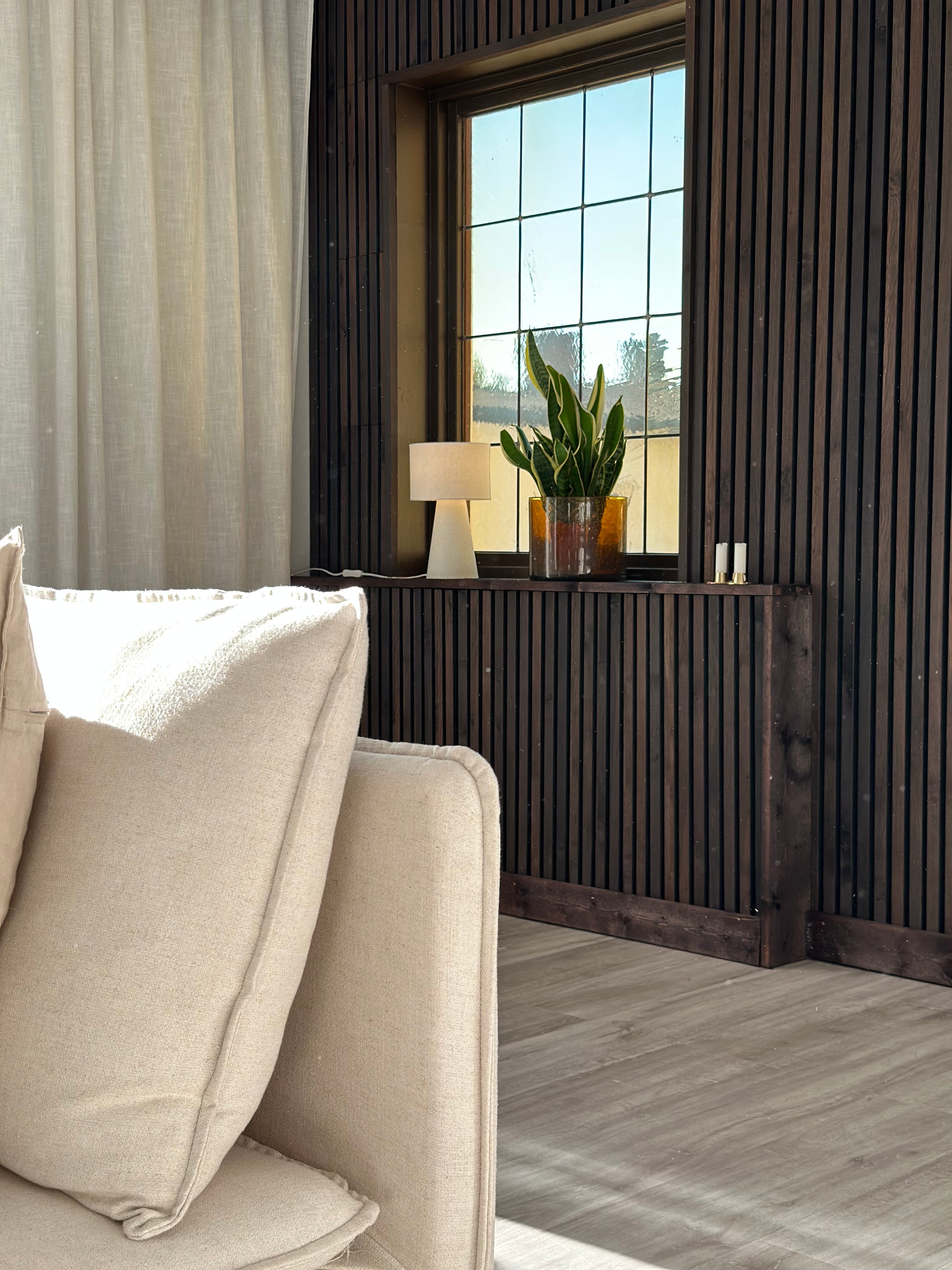 Dark wood Akupanel acoustic slat panels framing a window with potted plant, table lamp and beige sofa