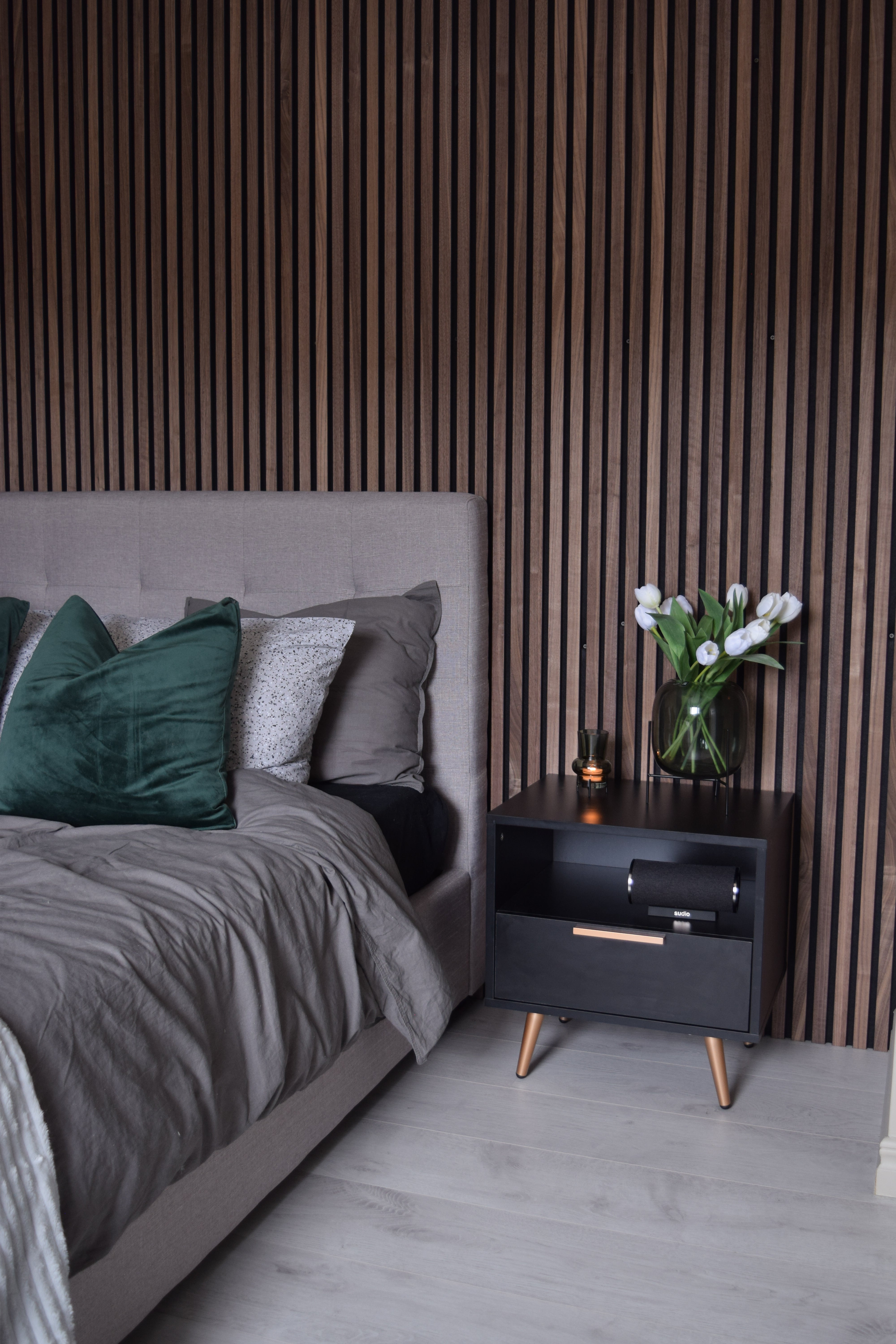 Walnut Akupanel acoustic slat wall panels behind a bed and nightstand in a bedroom.