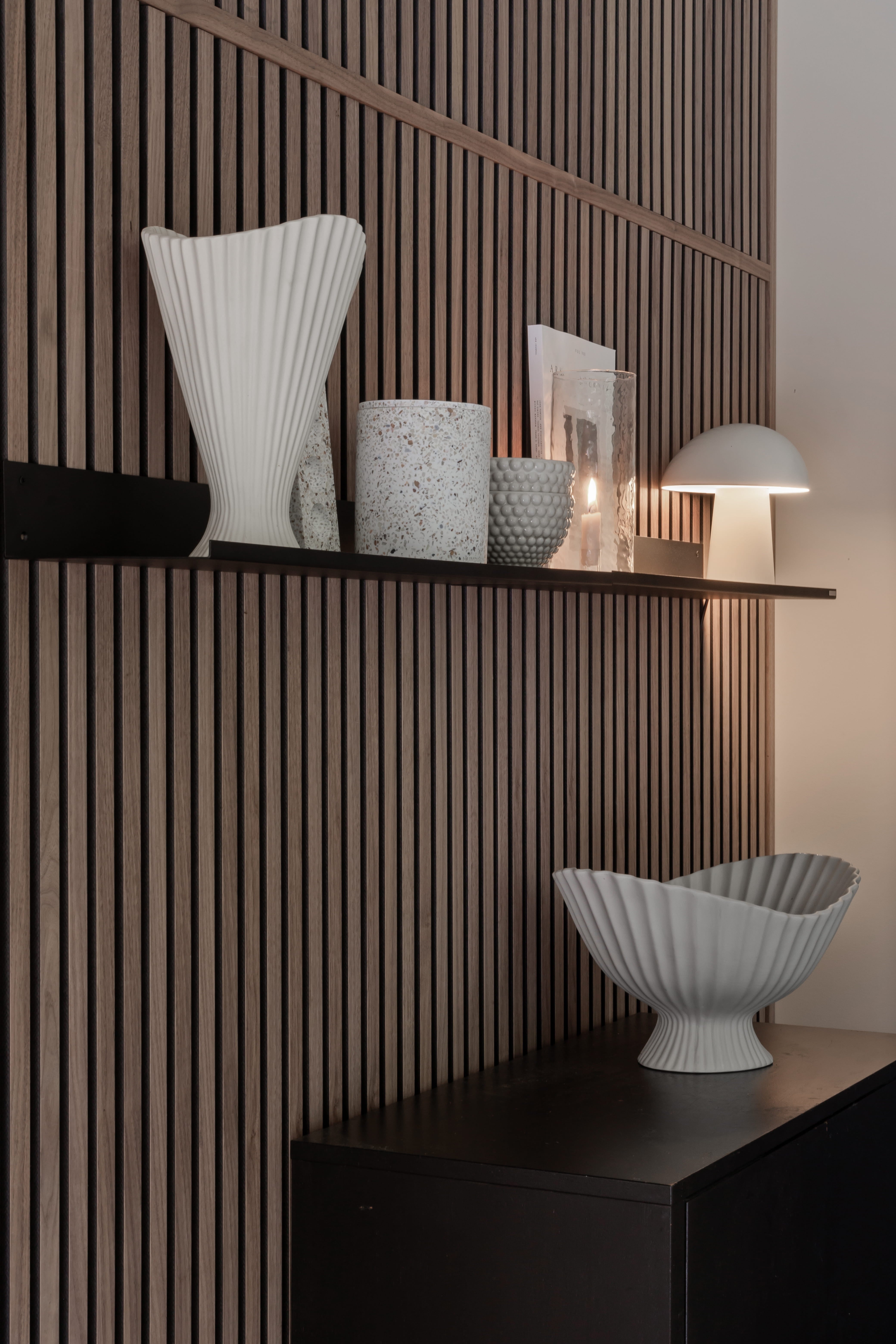 Walnut Akupanel acoustic slat wall panels behind a black shelf with vases and a lit lamp