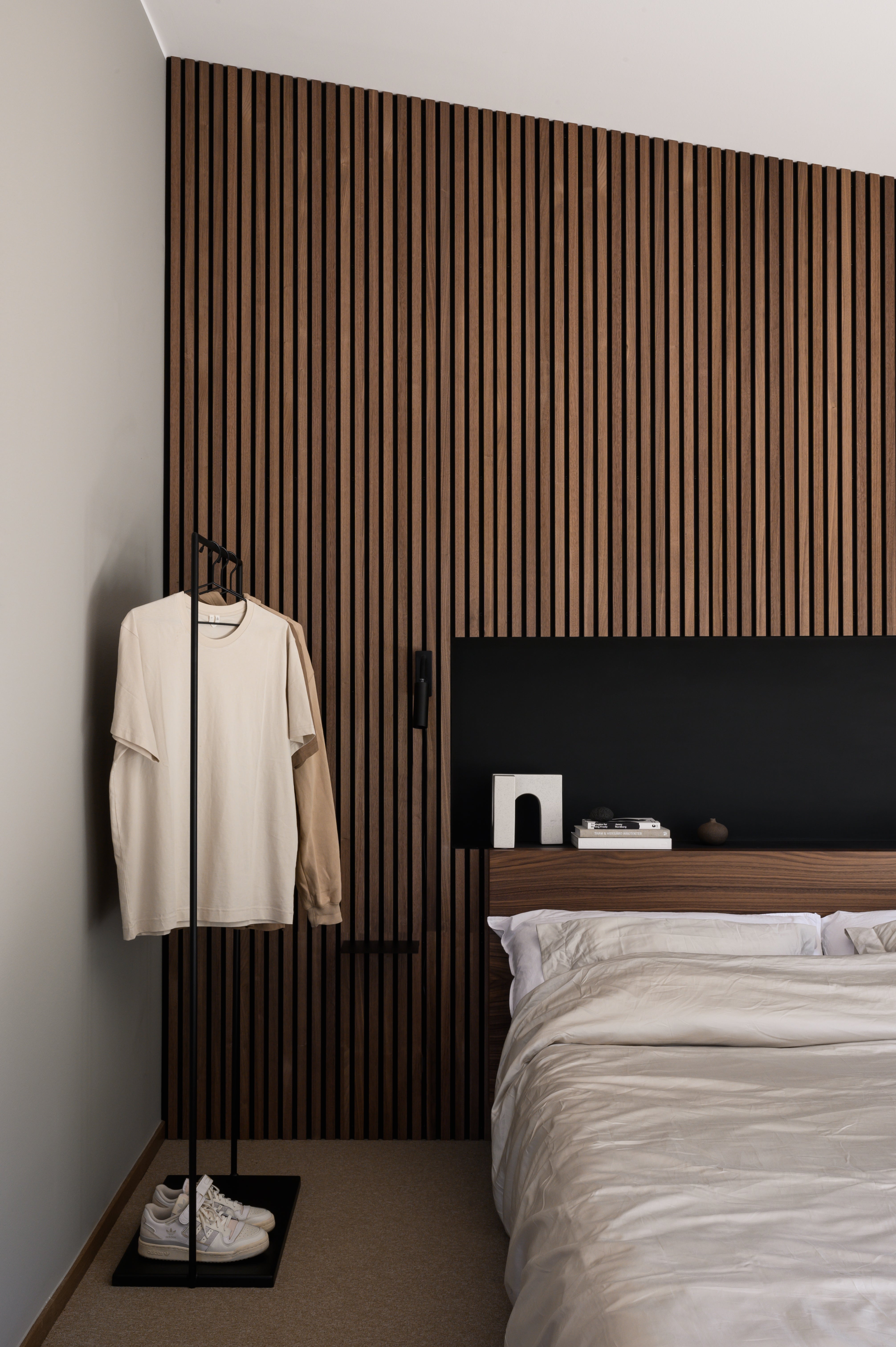 Walnut Akupanel acoustic slat wall behind bed with beige bedding, clothes rack and decor on wooden headboard