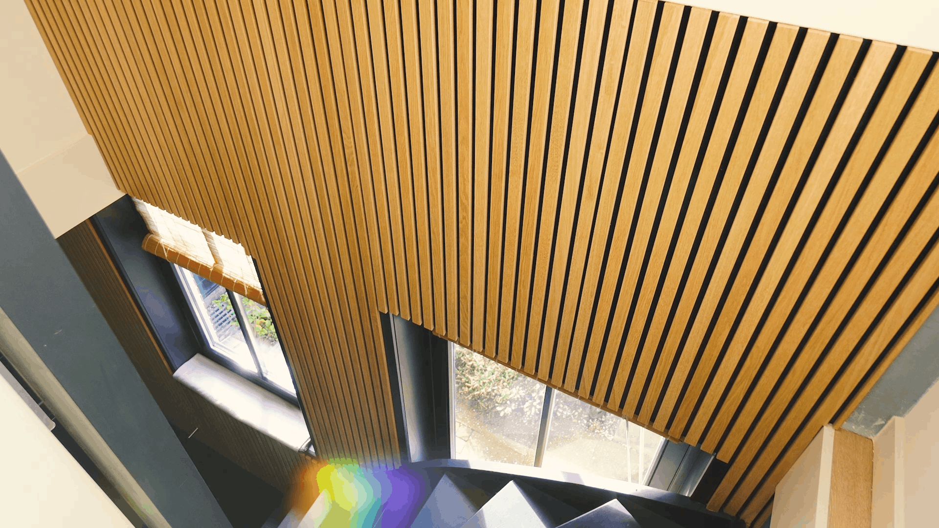 Light wood Akupanel acoustic slat panels with black backing on interior stairwell wall and ceiling.