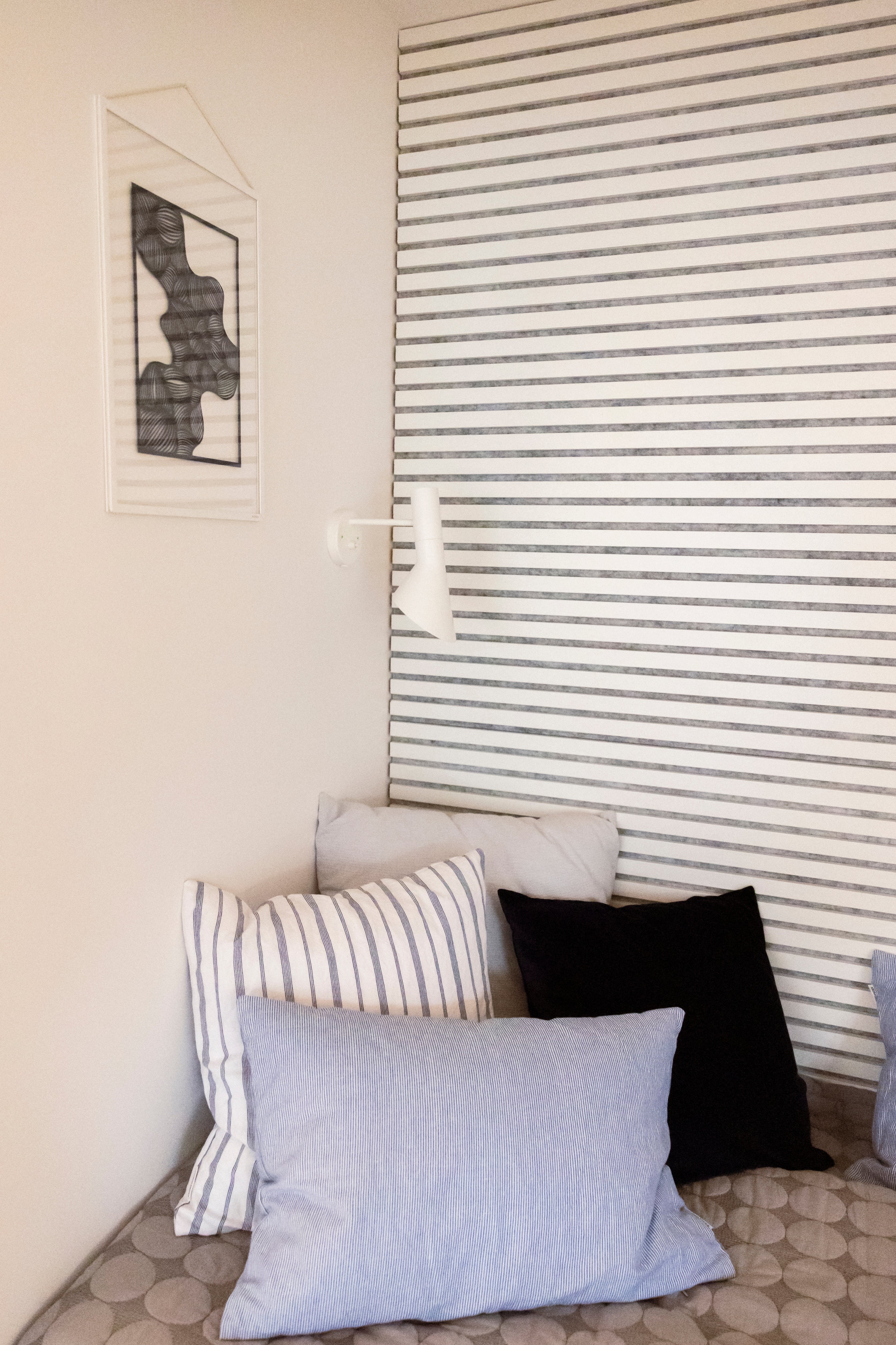 A cozy corner with patterned pillows, a wall lamp, striped acoustic panel decor, and a striped Akupanel accent wall for added visual interest.