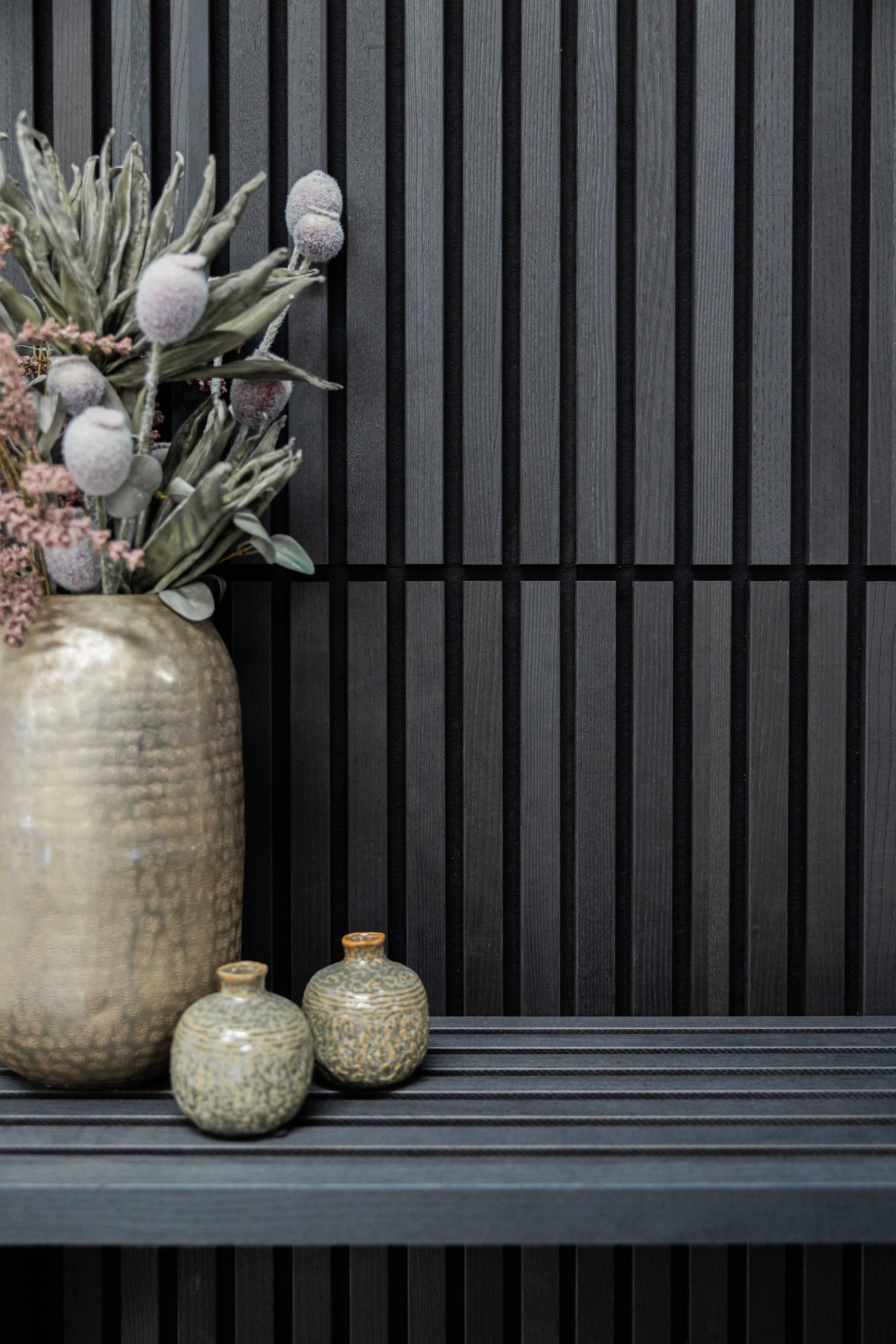 Black Akupanel acoustic slat wall panels with metallic vases and dried flowers on a slatted shelf