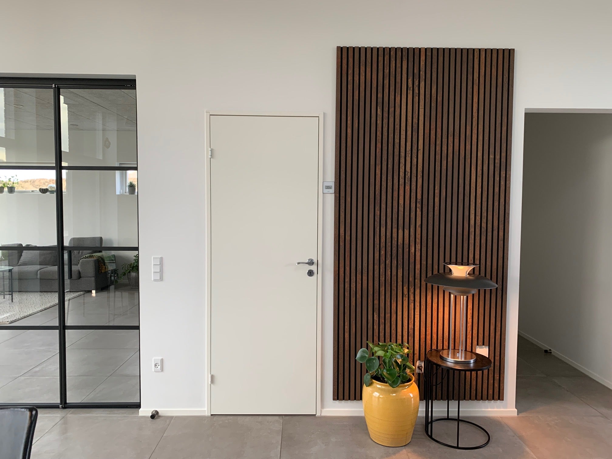 Dark wood Akupanel acoustic slat wall panel on white interior wall beside door and glass partition.