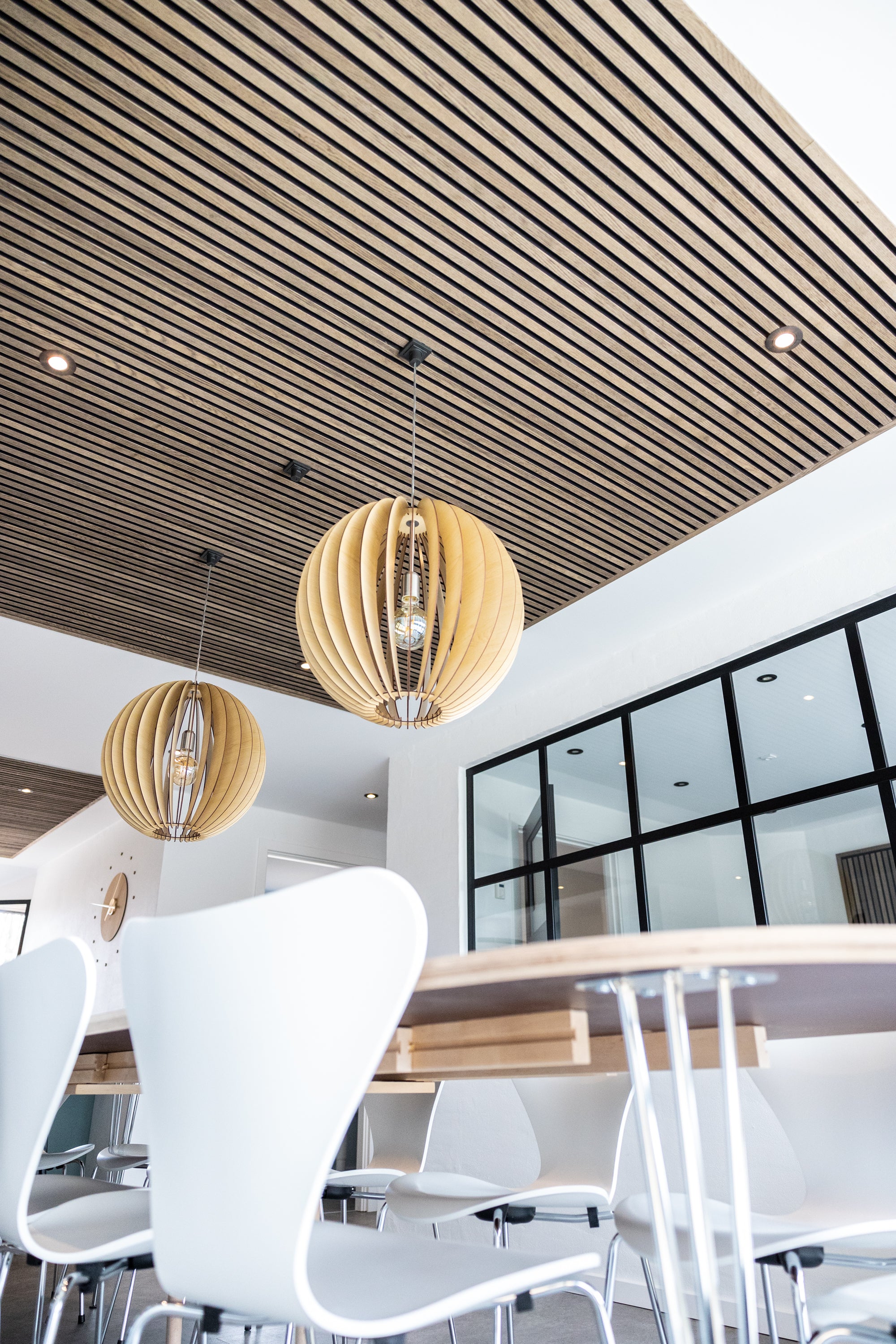 Akupanel acoustic wood slat ceiling panels with black backing above a dining area.