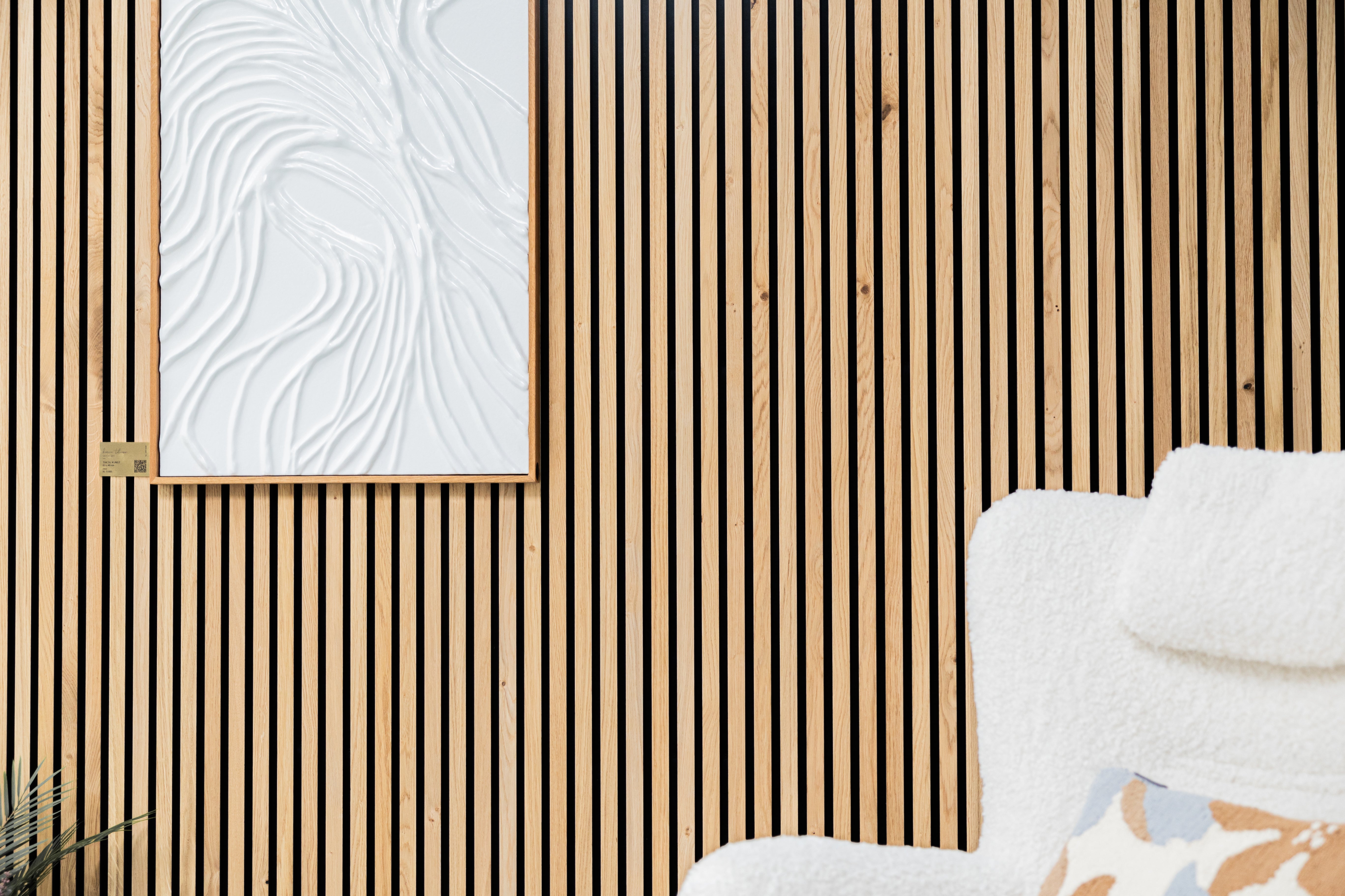 Akupanel wood slat acoustic wall with black backing, framed white textured panel and corner of a white fuzzy chair