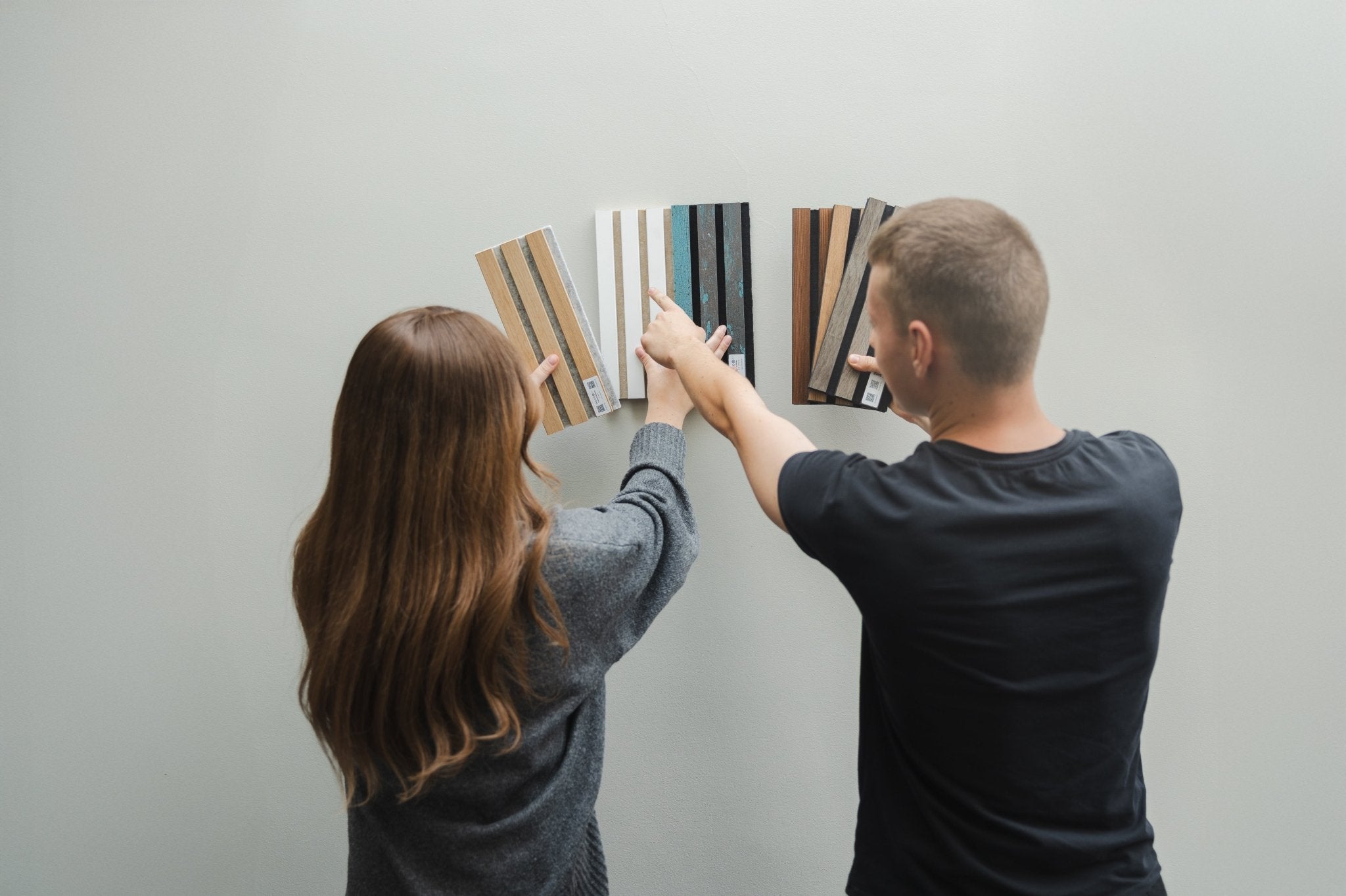 Akupanel slat sample boards held by two people against a plain light grey wall