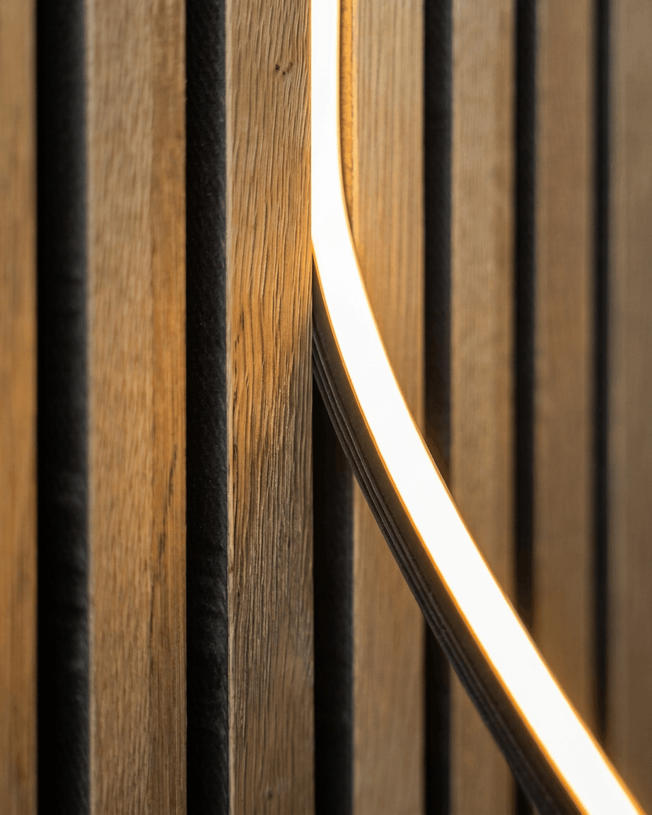 Close-up of the Lumi LED striplight (240 cm, Black) by WoodUpp installed on a Nordic Akupanel acoustic wood panel; Philips Hue compatible.