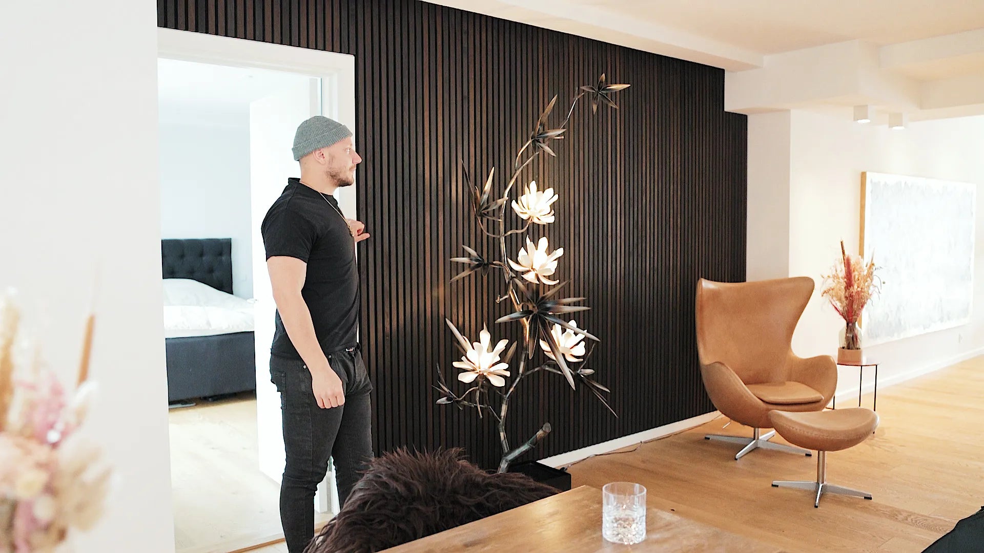Black Akupanel acoustic slat wall panels in living room with man, floral floor lamp and tan lounge chair.