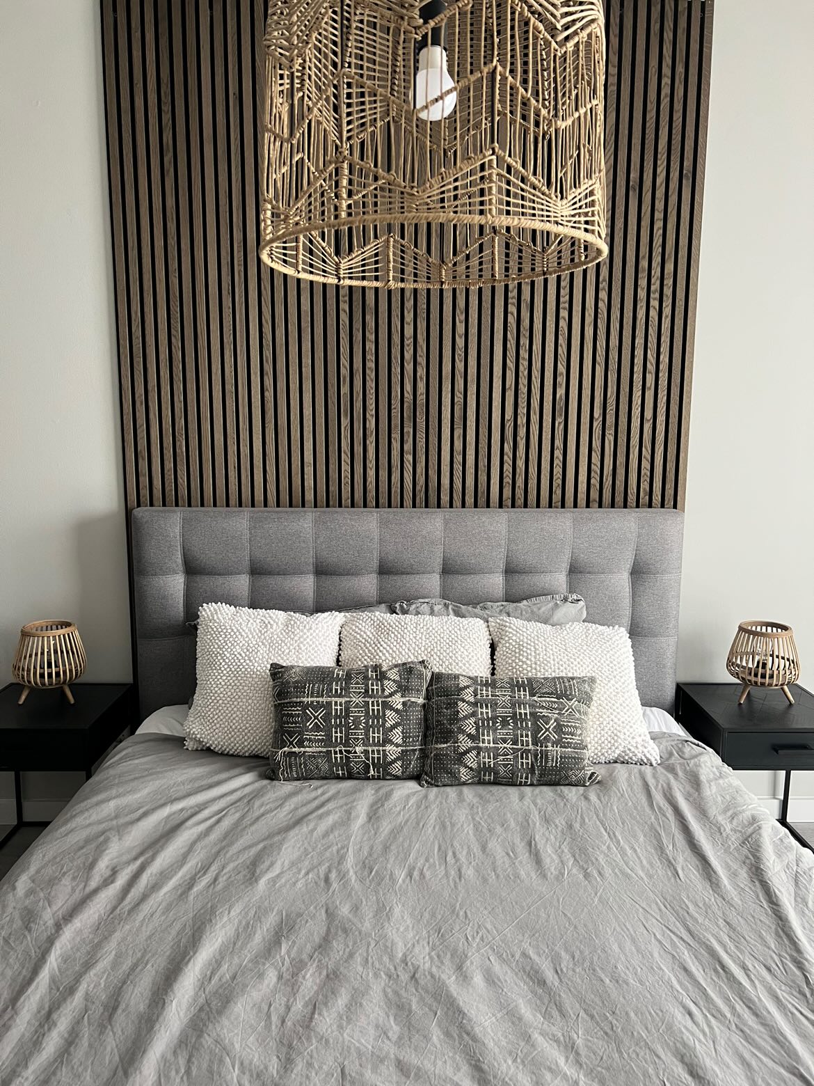 Akupanel acoustic wood slat wall panels on black backing behind a grey upholstered bed.